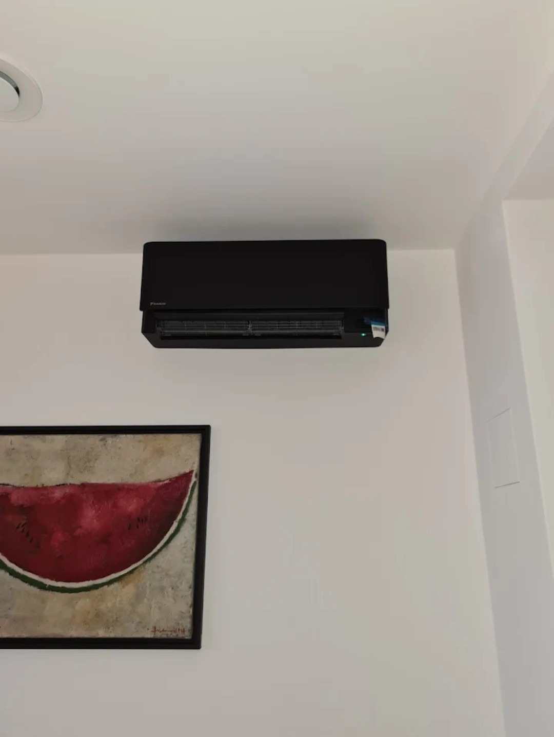 Czarny klimatyzator ścienny Daikin zamontowany w pomieszczeniu z obrazem arbuza na ścianie.