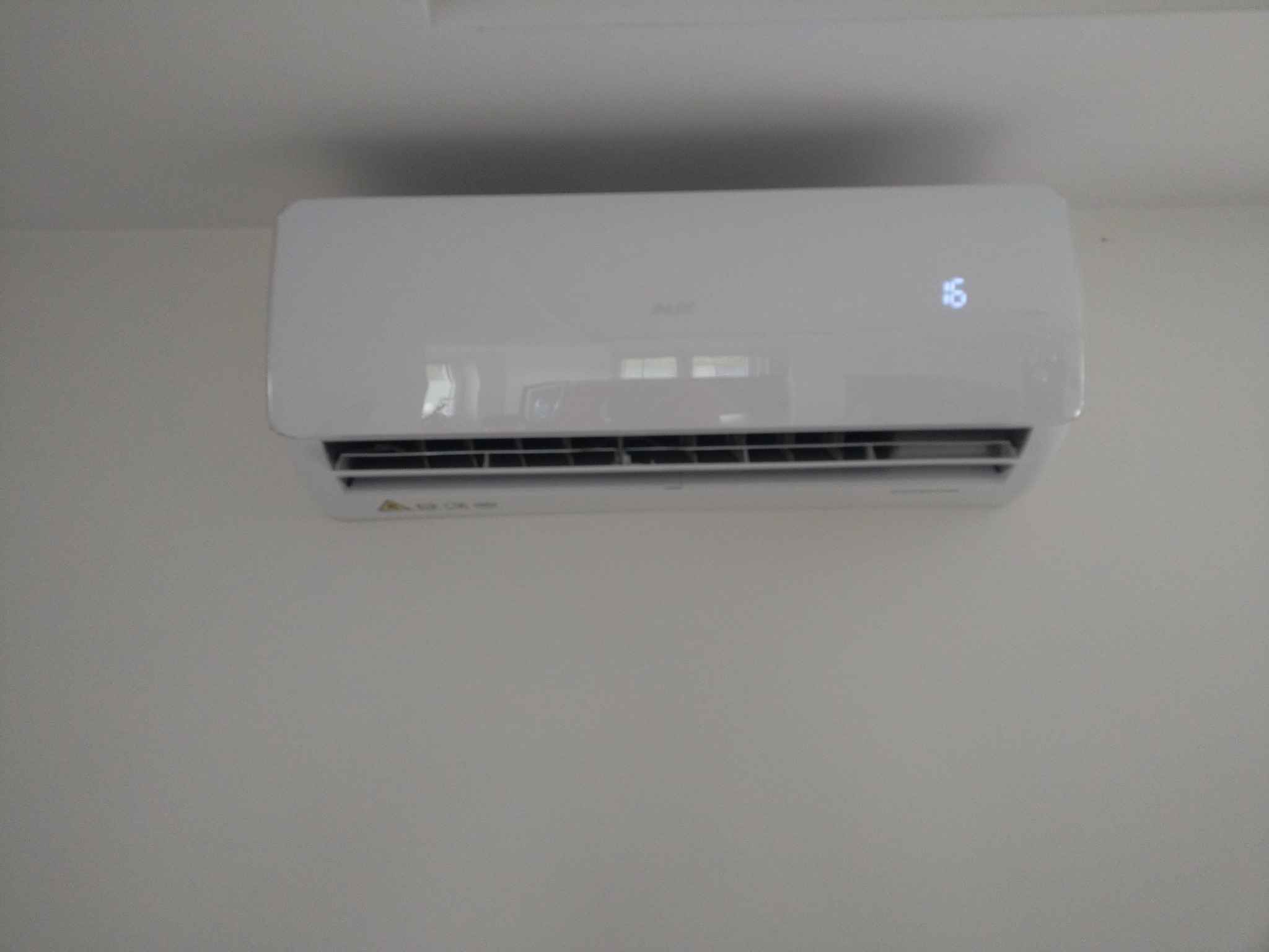 Biały klimatyzator marki AUX zamontowany na jasnej ścianie, wyświetlający temperaturę 16 stopni Celsjusza.