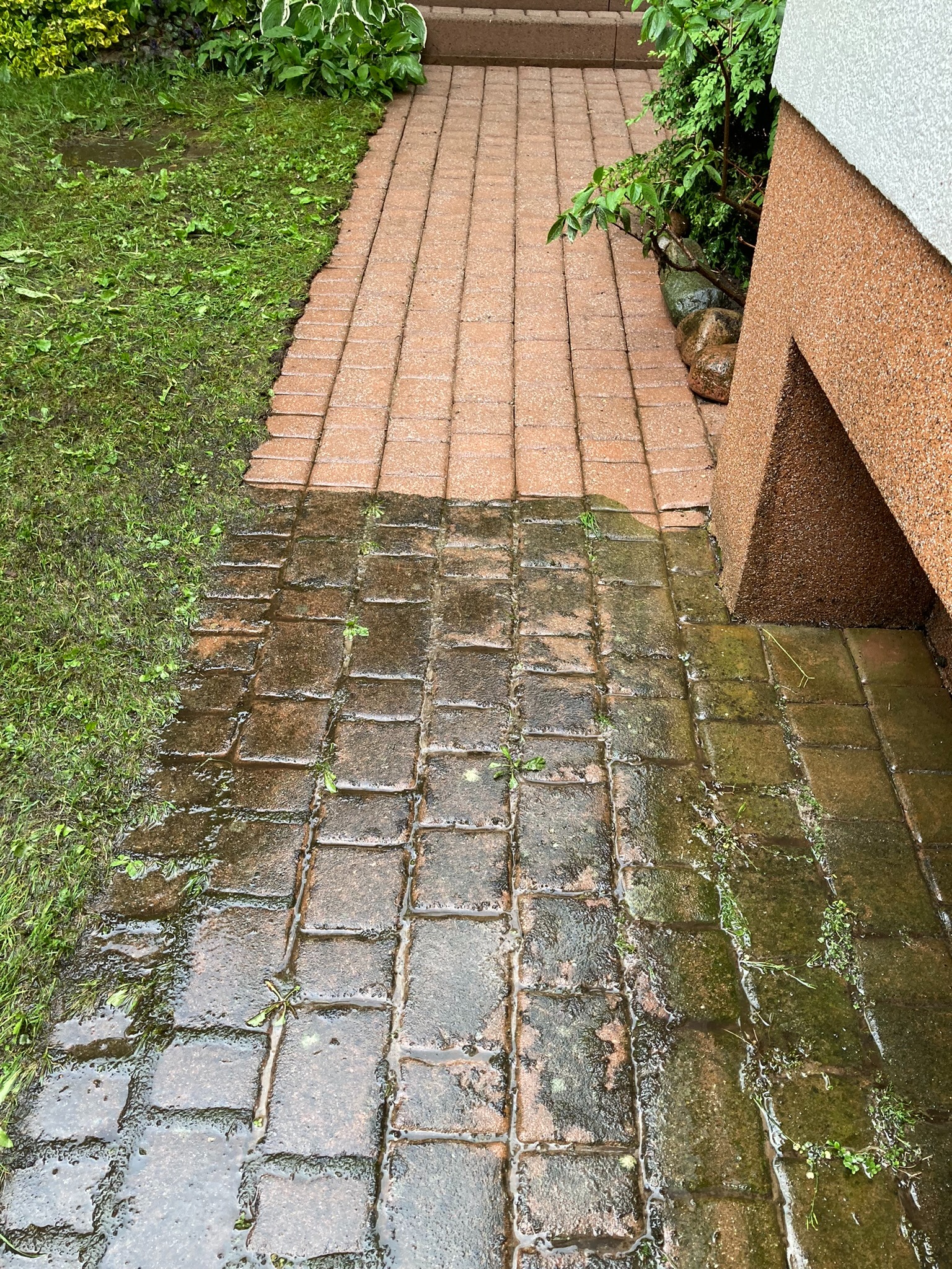 Częściowo umyta, mokra kostka brukowa przed domem, widoczna różnica w czystości między umytą a nieumytą powierzchnią.