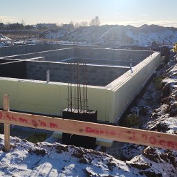 SOLID HAUS ADAM KOSATER - Fundamenty domu jednorodzinnego ocieplone styropianem, widoczne zbrojenia i drewniane szalunki z oznaczeniami, zimowy krajobraz w tle.