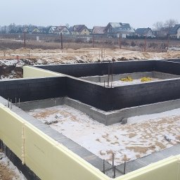 SOLID HAUS ADAM KOSATER - Fundamenty domu jednorodzinnego w Nowej Karczmie, z izolacją termiczną i zbrojeniami, na tle zabudowy mieszkalnej w pochmurny dzień.