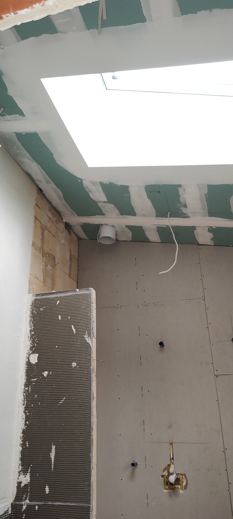 Wnętrze w trakcie wykończenia: płyty gipsowe na ścianach i suficie, widoczne instalacje, przygotowanie podłoża pod płytki. Otwór okienny w suficie.