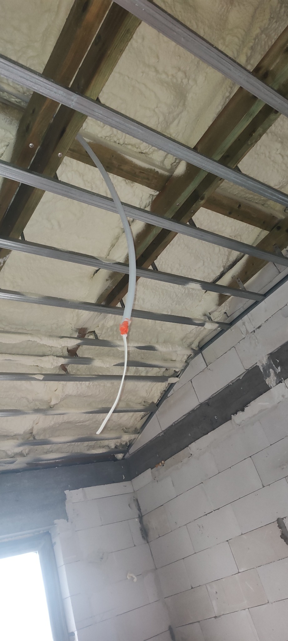 Poddasze z drewnianą konstrukcją, ocieplone pianą PUR, z widoczną rurką instalacyjną. Ściany z białych bloczków. Widok z dołu, ukośne ujęcie.