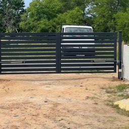 PanelExpress Ogrodzenia - Nowoczesna, pozioma brama wjazdowa z automatyką, widoczna z bliska na tle zieleni i zaparkowanego białego busa. Widoczne narzędzia montażowe.