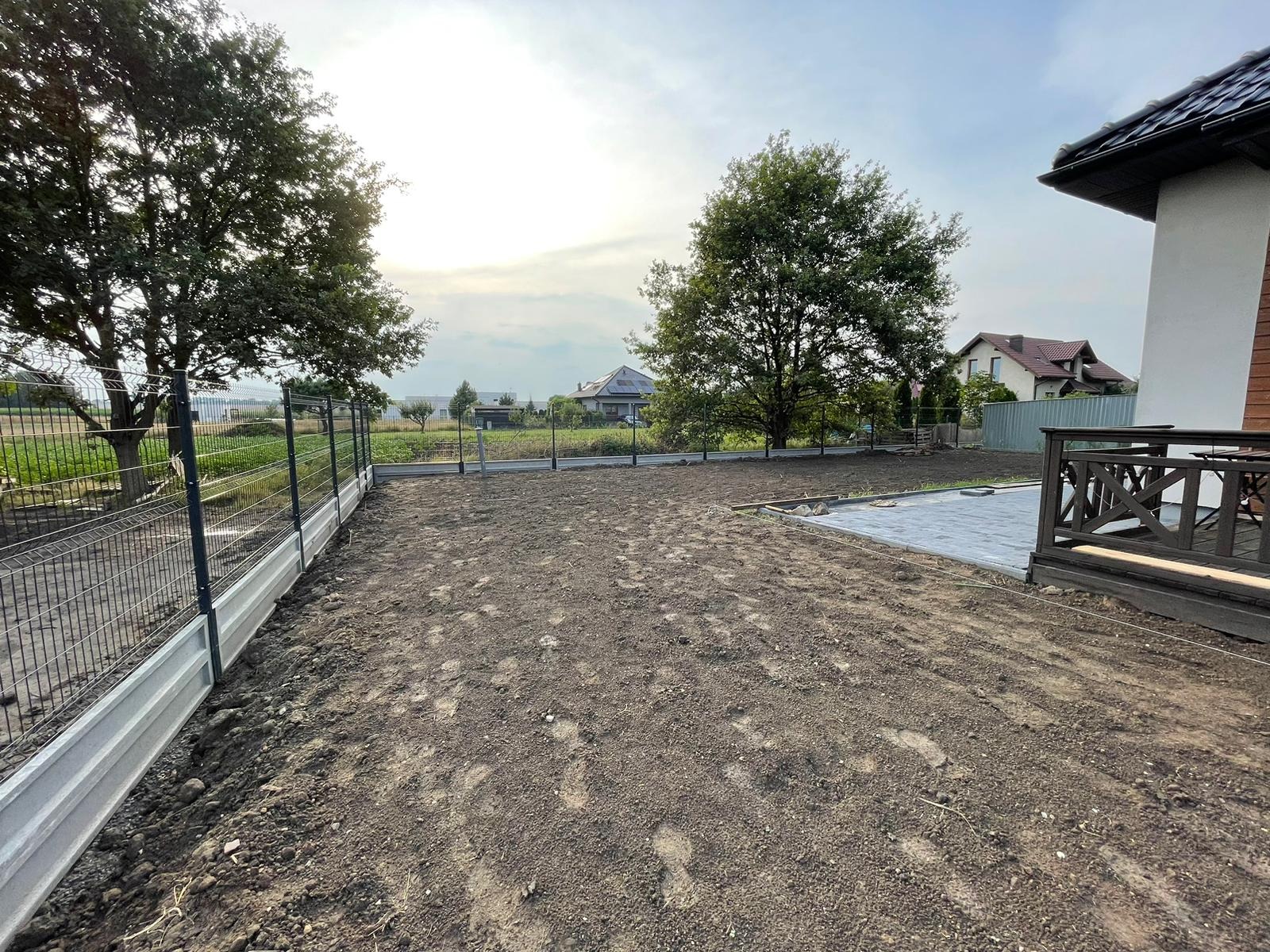 Nowo zamontowane ogrodzenie panelowe z betonową podmurówką na działce z przygotowanym terenem pod trawnik, widoczne ślady stóp na ziemi.