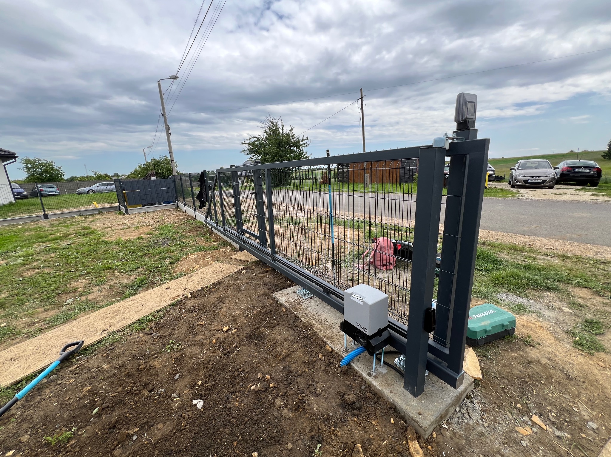 Montaż przesuwnej bramy panelowej z automatyką. Widoczny napęd FAAC 740, skrzynka Parkside, wykopana ziemia i częściowo zamontowane ogrodzenie panelowe.