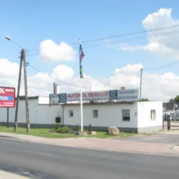 Budynek warsztatu samochodowego Autopol Service z reklamą usług: mechanika, zbieżność, oleje, klimatyzacja, sklep, okręgowa stacja kontroli pojazdów. Na dachu baner z napisem Autopol Service...