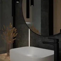 Nowoczesna łazienka z białą, prostokątną umywalką nablatową, czarną armaturą i okrągłym lustrem z podświetleniem LED, uzupełniona dekoracyjnym bukietem suszonych traw w szklanym wazonie.