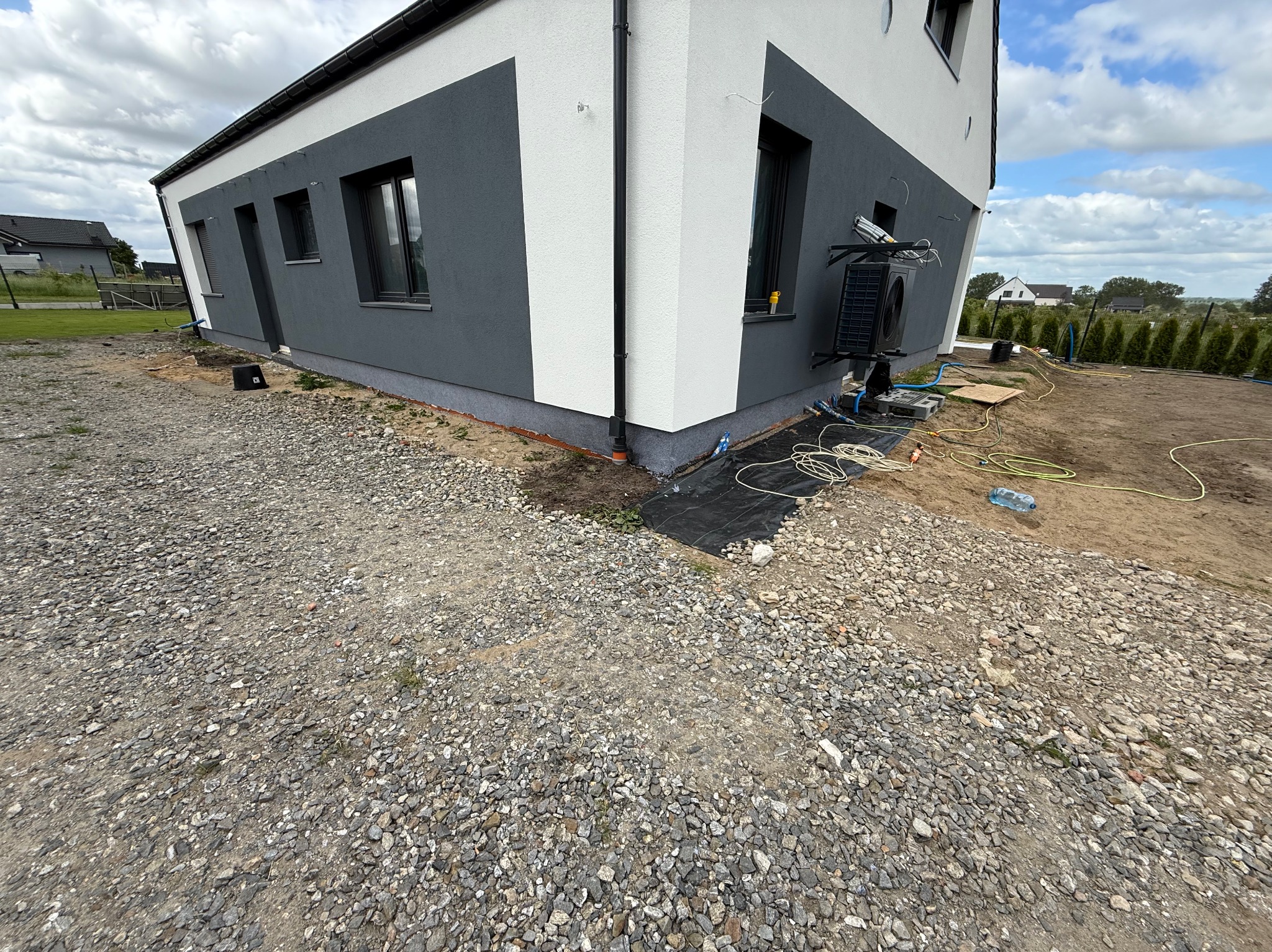 Nowoczesny dom z elewacją w odcieniach szarości i bieli, widok z zewnątrz. Uwagę zwraca kontrast kolorów i minimalistyczny design. Widoczne elementy instalacji zewnętrznej.