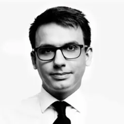 Portret biznesowy mężczyzny w okularach, czarno-biały, z delikatnym uśmiechem i ciemnym krawatem o wyraźnej fakturze.