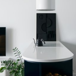 SUSPENS studio - Nowoczesna kuchnia z wyspą w odcieniach bieli i granatu, minimalistyczna dekoracja ścienna i czajnik na blacie. Roślina doniczkowa dodaje świeżości.