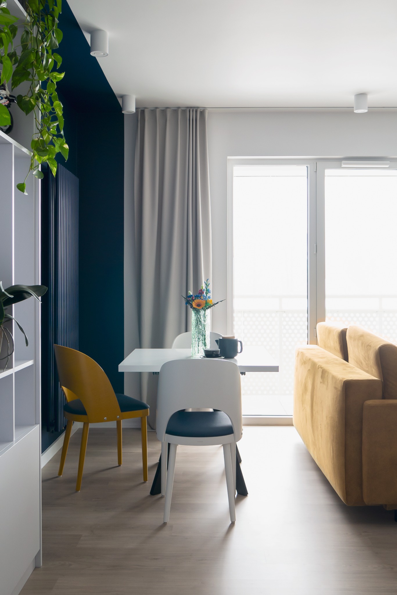 Nowoczesna aranżacja wnętrza: stół z kwiatami, krzesła w kolorze musztardowym i granatowa ściana. Minimalistyczny design z jasnym parkietem.