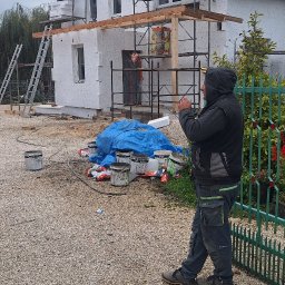 REM-SAR - Dom jednorodzinny w trakcie prac związanych z izolacją termiczną ścian zewnętrznych, widoczne rusztowania, styropian, puszki z klejem i pracownik w odzieży roboczej