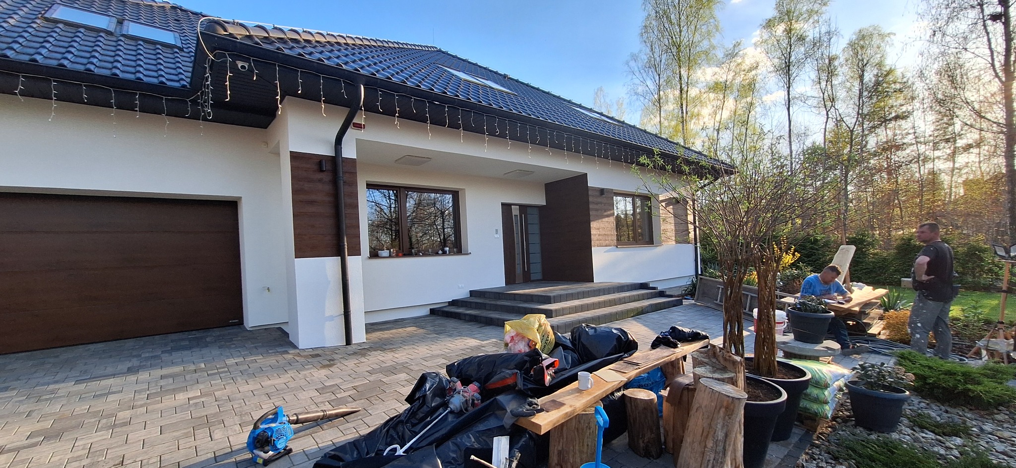 Nowoczesny dom jednorodzinny w Solcu-Zdroju po wykonaniu elewacji, z widocznymi elementami dekoracyjnymi i ciemną stolarką okienną. Na pierwszym planie materiały budowlane i narzędzia.