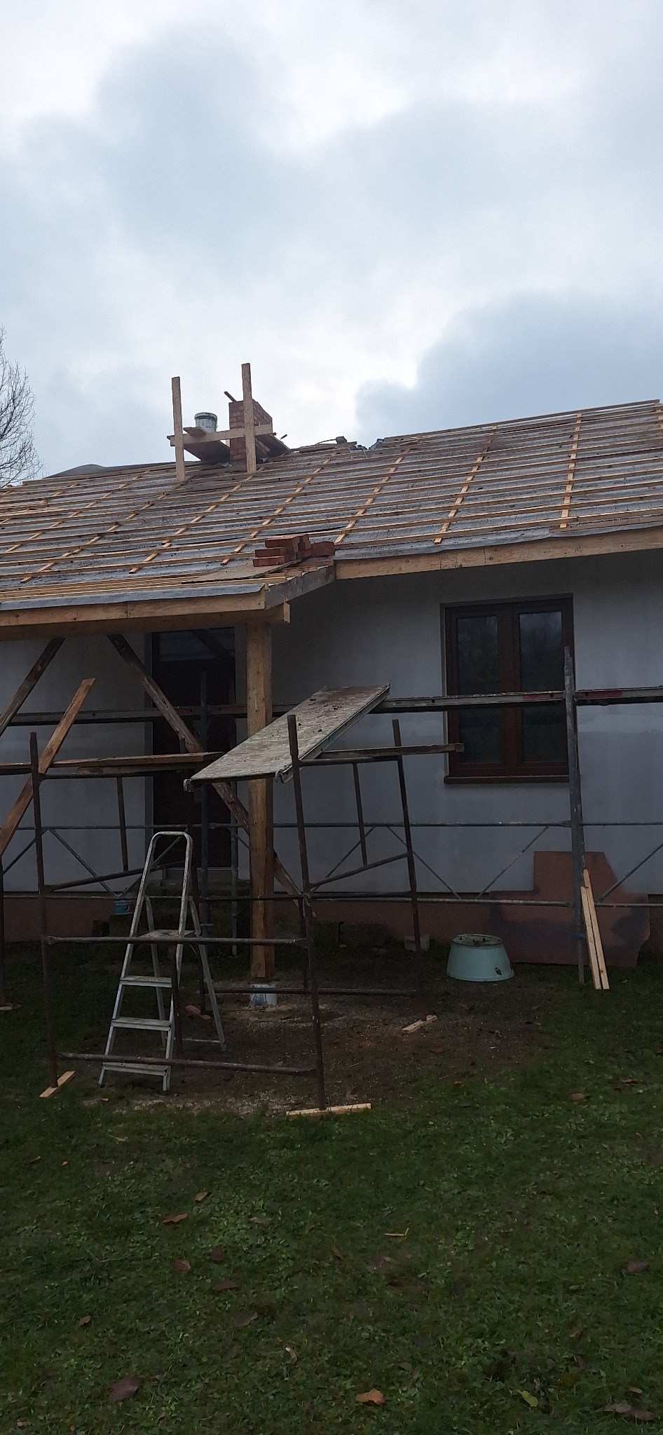 Dom jednorodzinny w trakcie budowy dachu, widoczne rusztowania, drabina i częściowo ułożona dachówka.