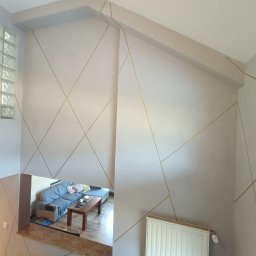 Pro Standard Bartłomiej Miczołek - Pomalowane ściany w geometryczne złote linie, widok na salon z poziomu schodów, grzejnik na ścianie, okno z luksferów.