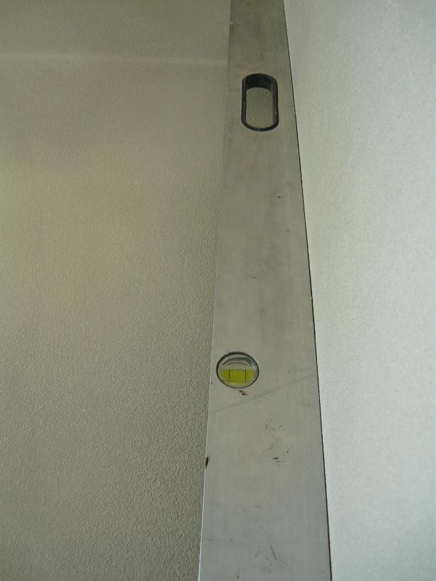 Poziomnica pionowo przyłożona do tynkowanej ściany w Szamotułach, kontrola pionu podczas prac tynkarskich.