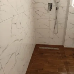 Kabina prysznicowa z białymi płytkami imitującymi marmur i drewnopodobną podłogą z odpływem liniowym.