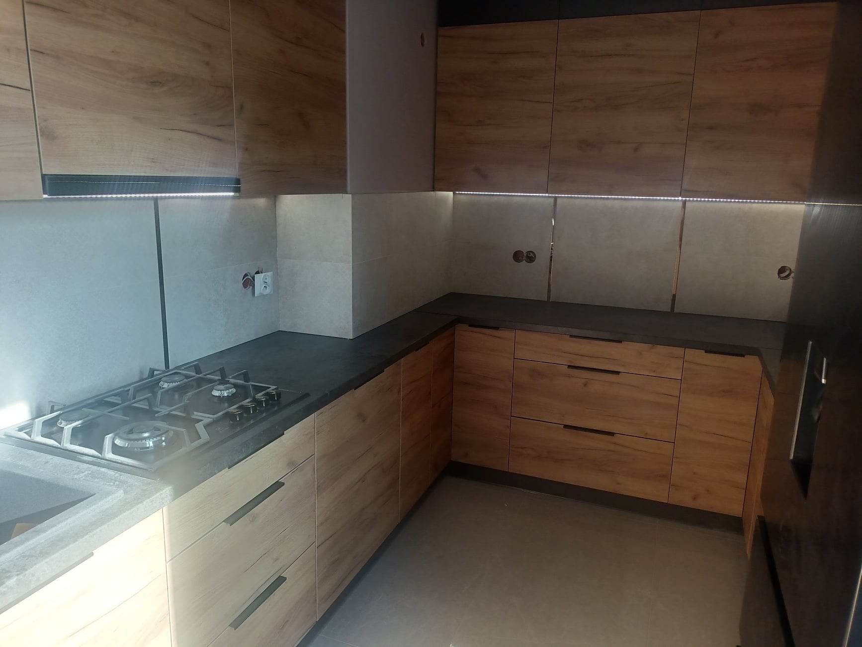 Nowoczesna kuchnia w odcieniach drewna i szarości, z podświetleniem LED podszafkowym i płytą gazową na blacie.