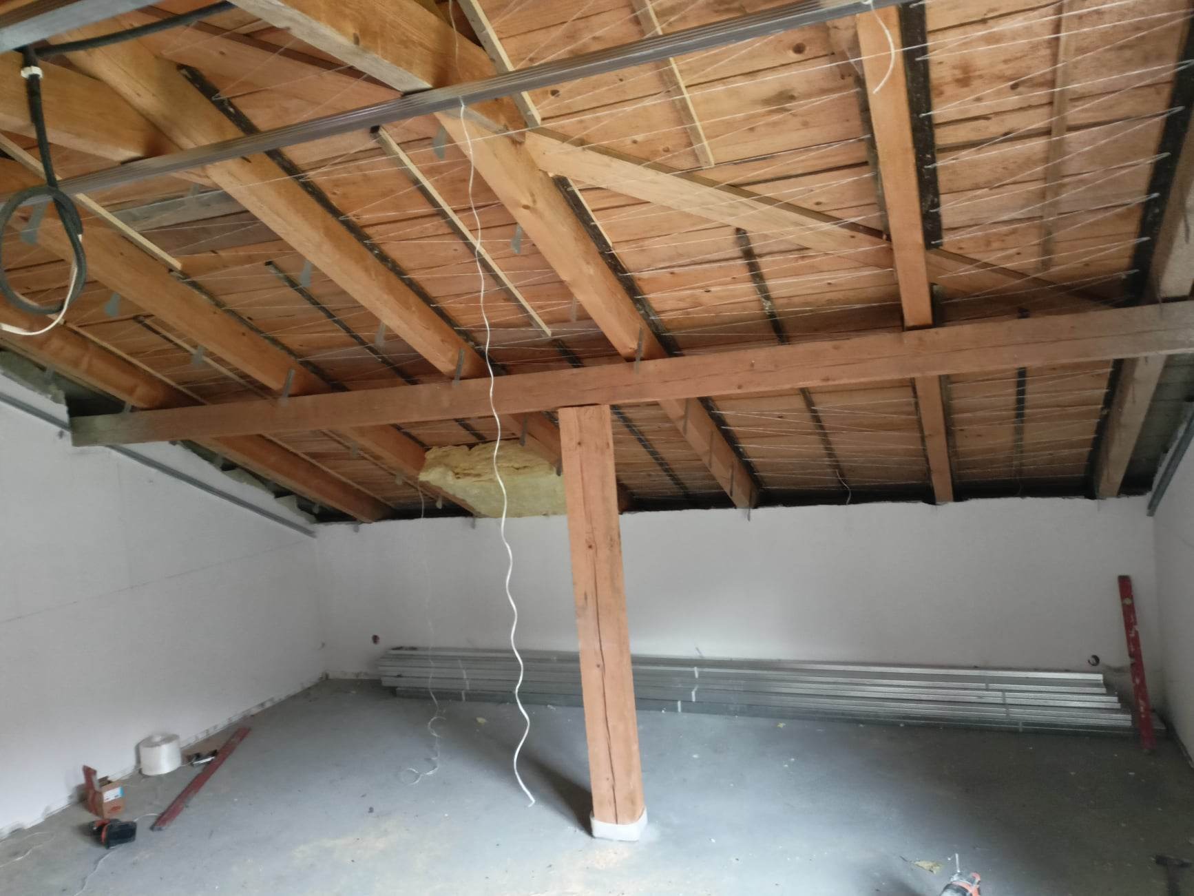 Poddasze w trakcie adaptacji: drewniana konstrukcja dachu z metalowymi profilami pod płyty karton-gips, częściowo ocieplone, białe ściany, przygotowane profile na podłodze, poziomica oparta o ścianę.