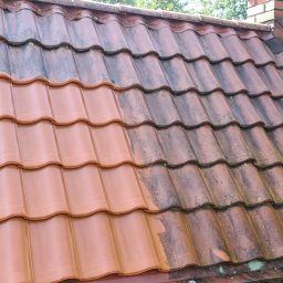 Cleanhouse_warszawa - Częściowo wyczyszczony dach z czerwonej dachówki ceramicznej, widoczna wyraźna różnica między umytą a brudną powierzchnią, komin w tle.
