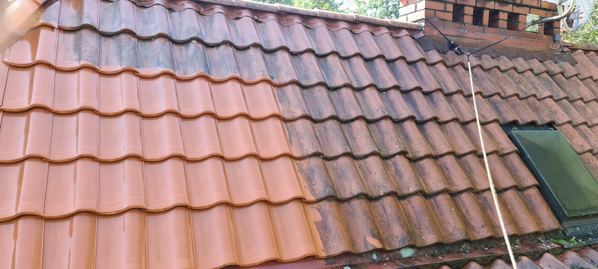 Częściowo wyczyszczony dach z czerwonej dachówki ceramicznej, widoczna wyraźna różnica między umytą a brudną powierzchnią, komin w tle.