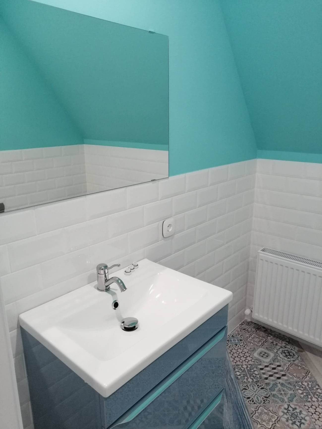 Nowoczesna łazienka na poddaszu z turkusowymi ścianami, białymi płytkami metra, umywalką w niebieskiej szafce i grzejnikiem.