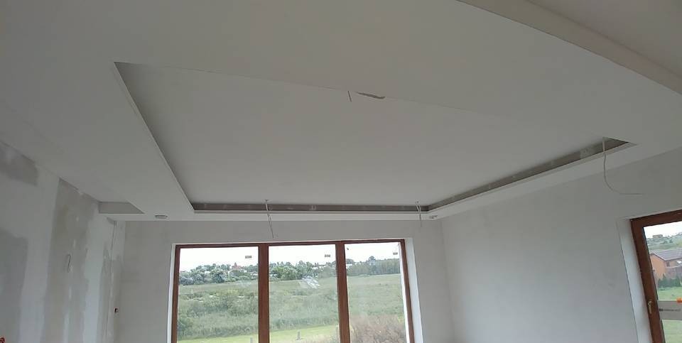 Nowoczesny sufit podwieszany z płyt kartonowo-gipsowych w jasnym wnętrzu, widoczne okna i niedokończone ściany.