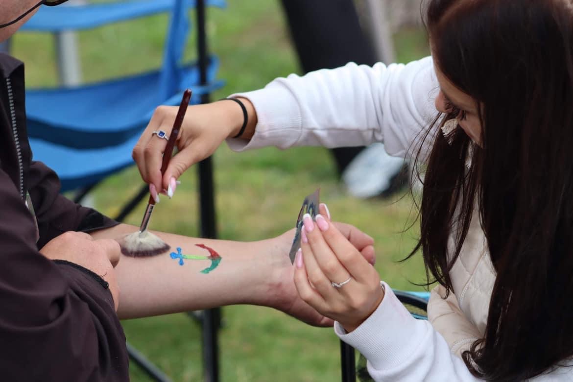 Malowanie farbami na skórze wzoru kotwicy przy użyciu pędzla i szablonu.