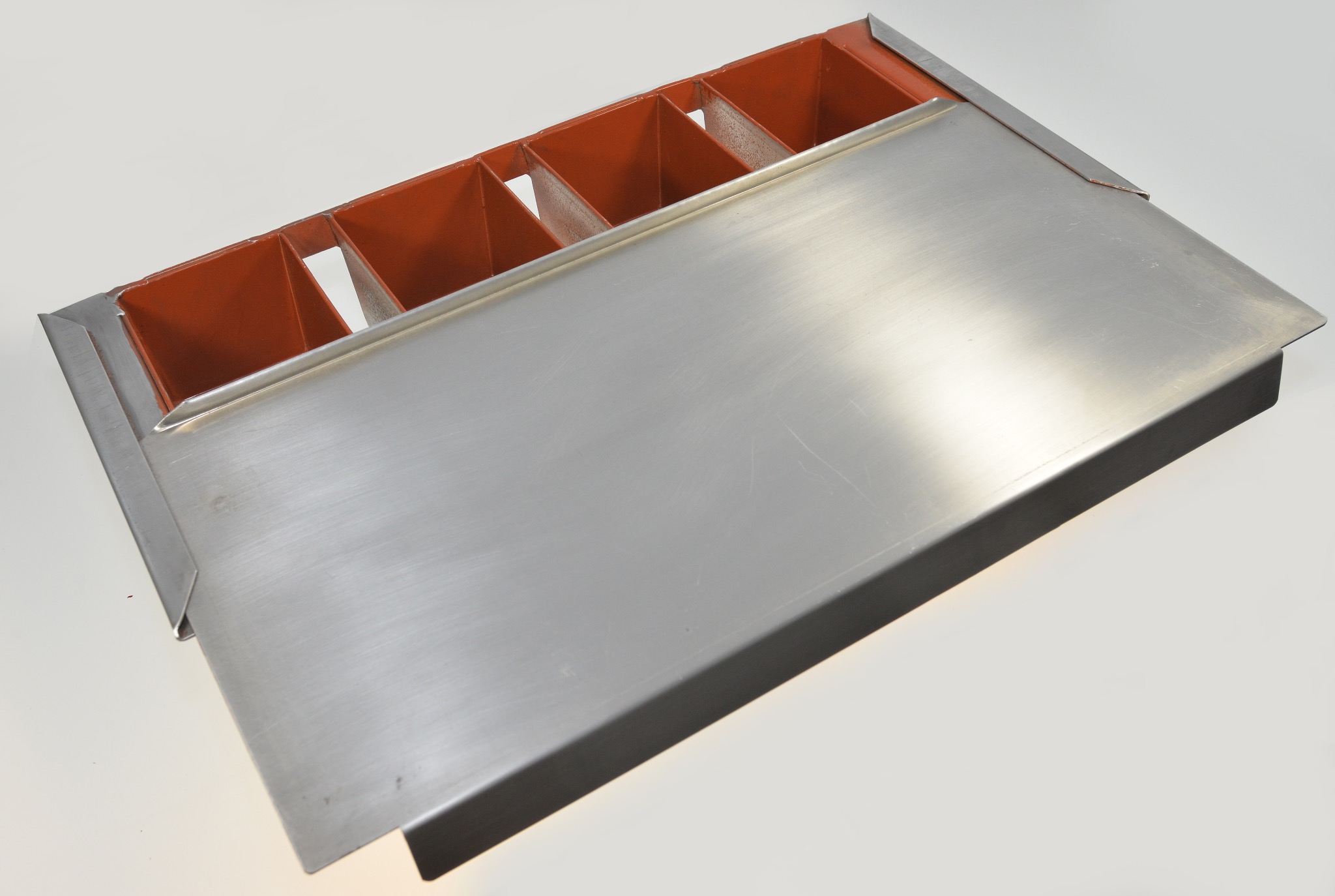 Metalowa konstrukcja z podziałem na segmenty i płaską powierzchnią, prawdopodobnie element odpływowy lub wentylacyjny, na białym tle.