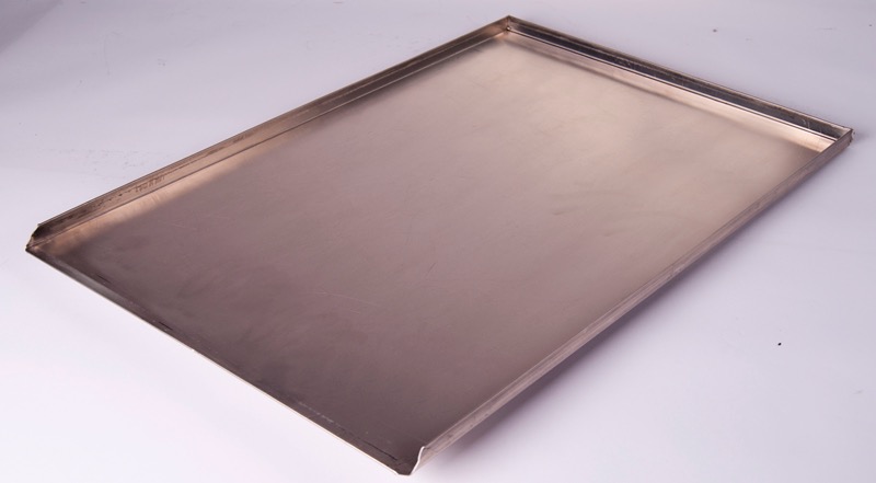 Prostokątna blacha ze stali nierdzewnej z zagiętymi brzegami, leżąca ukośnie na białym tle, widoczne delikatne refleksy światła.