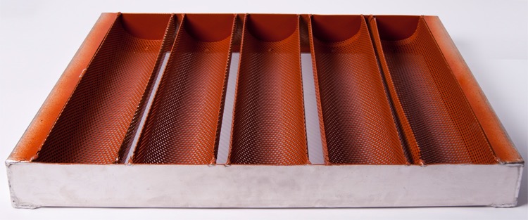 Perforowana forma do pieczenia bagietek z sześcioma zagłębieniami, pomarańczowo-srebrna, widoczna faktura siatki i ślady użytkowania.