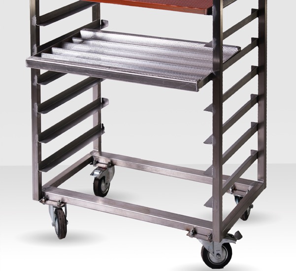Wózek gastronomiczny ze stali nierdzewnej na kółkach, z perforowanym blatem i prowadnicami na tace, oświetlony studyjnie na jednolitym tle.