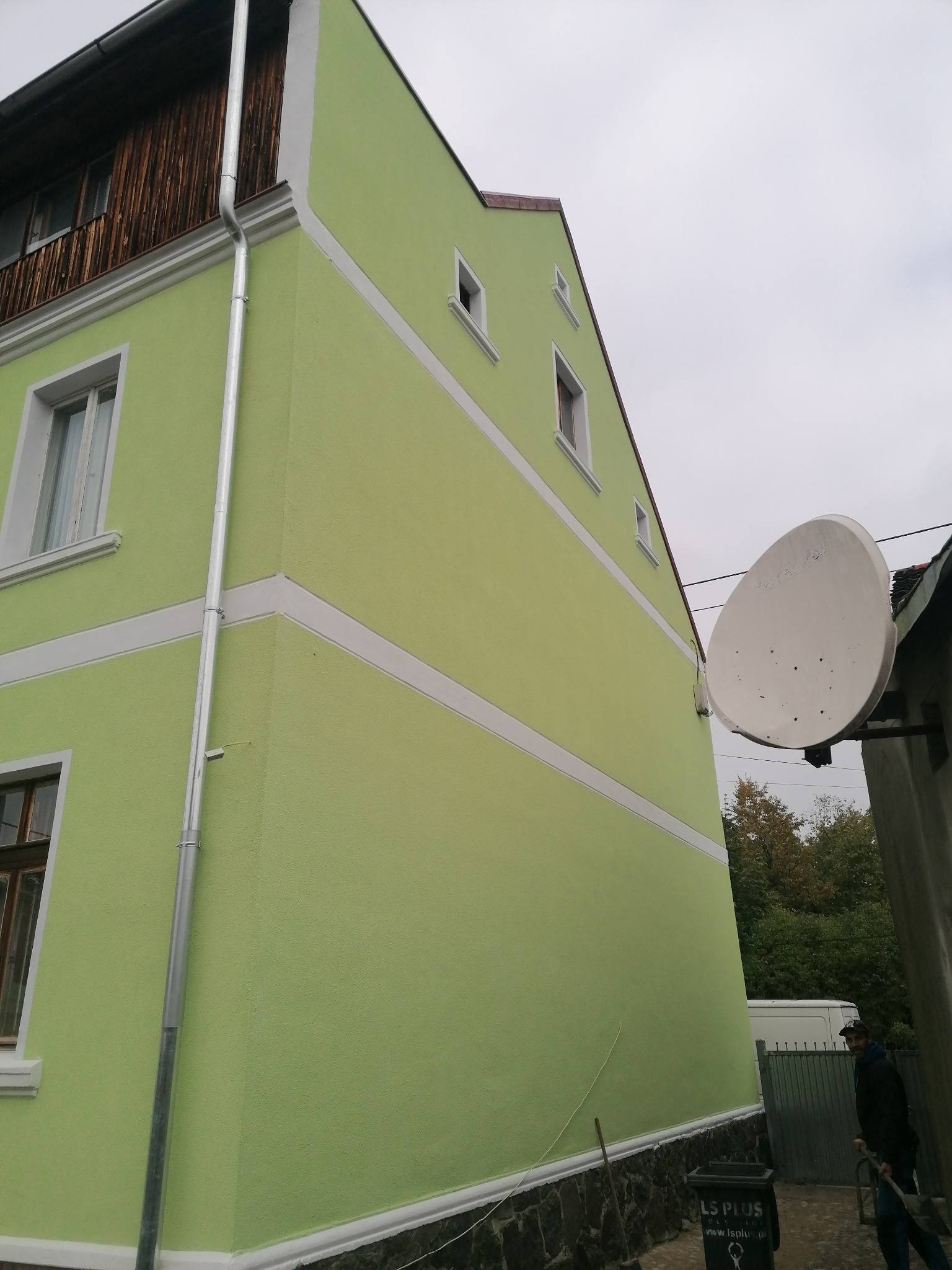 Odnowiona elewacja domu w odcieniach zieleni z białymi detalami, widoczna rynna spustowa i antena satelitarna na sąsiednim budynku.