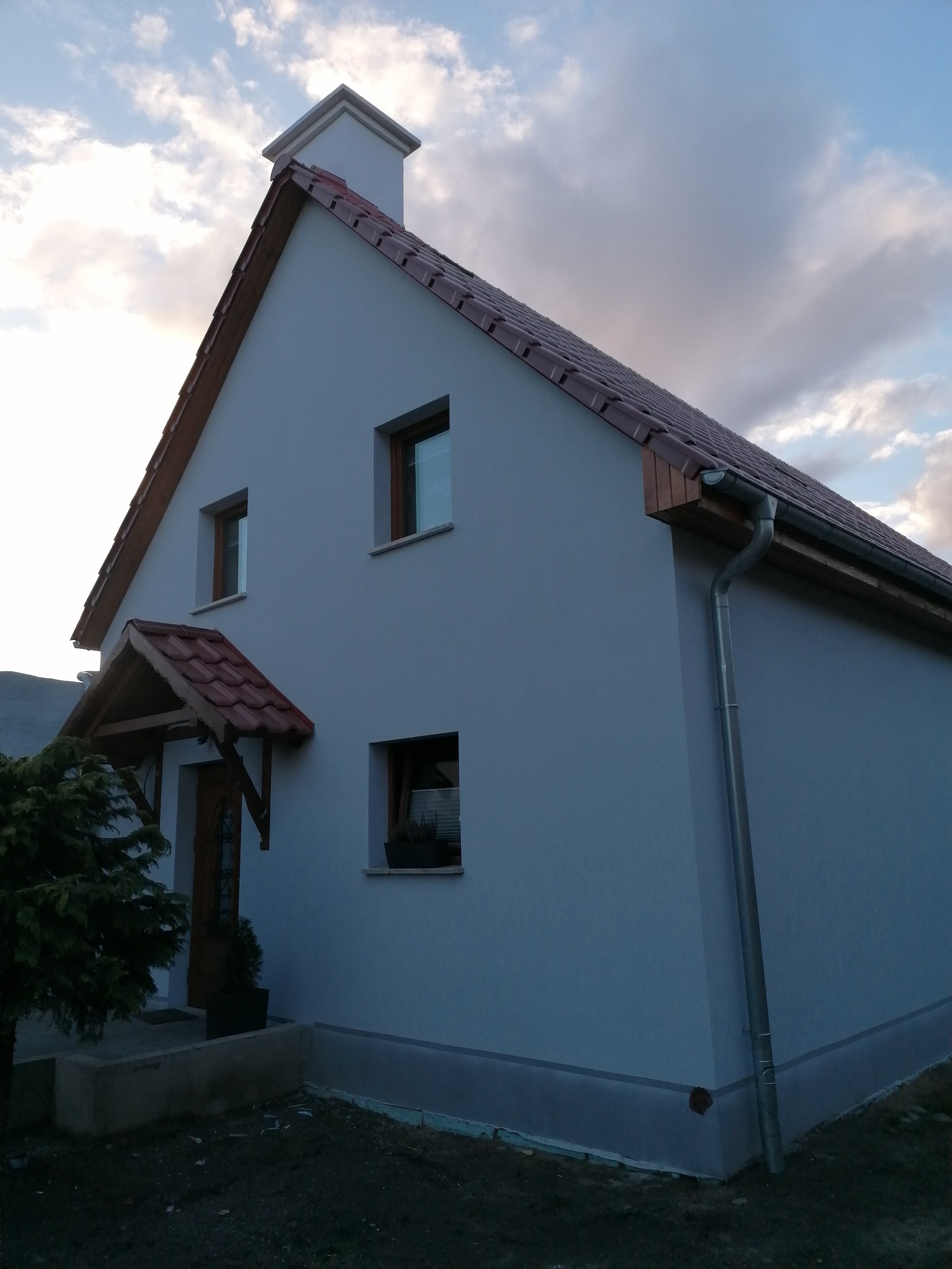 Dom jednorodzinny w Międzyrzeczu z nową, brązową dachówką i szarymi ścianami elewacji, widoczne rynny i niewielki daszek nad wejściem.