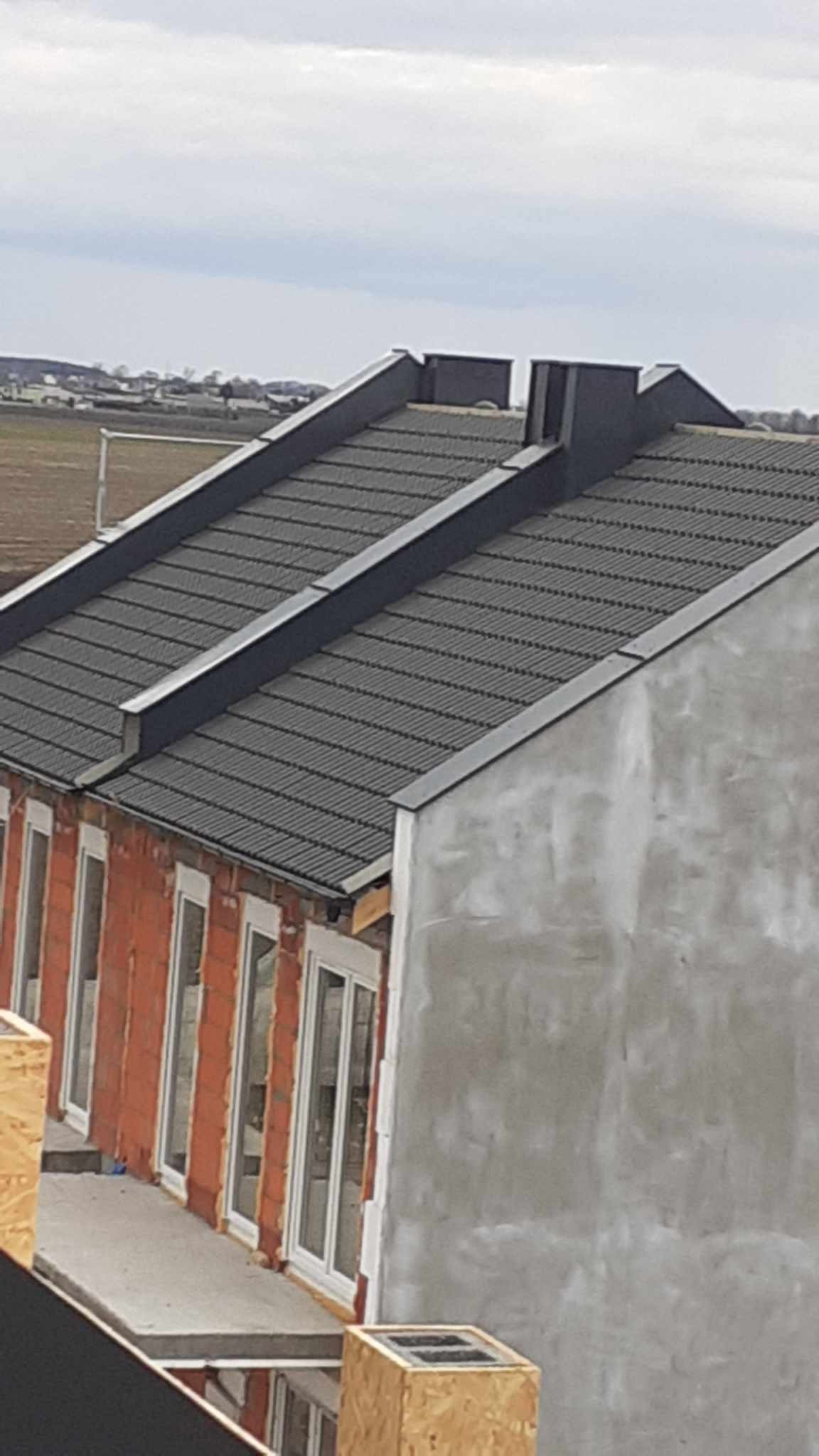 Nowy, ciemnoszary dach z blachy trapezowej na budynku w trakcie budowy, widoczne surowe ściany i okna.