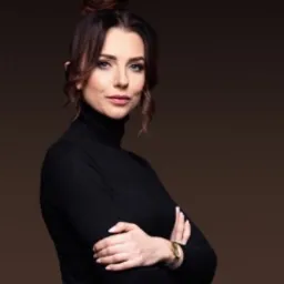 Portret kobiety z upiętymi włosami, ubrana w czarny golf, na ciemnobrązowym tle.