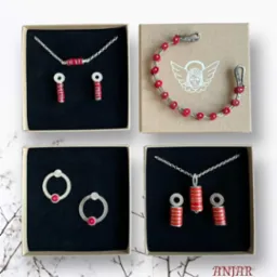 Cztery kwadratowe pudełka z biżuterią: naszyjniki, kolczyki i bransoletka z czerwonymi i srebrnymi elementami, prezentowane na tle z gałązkami.