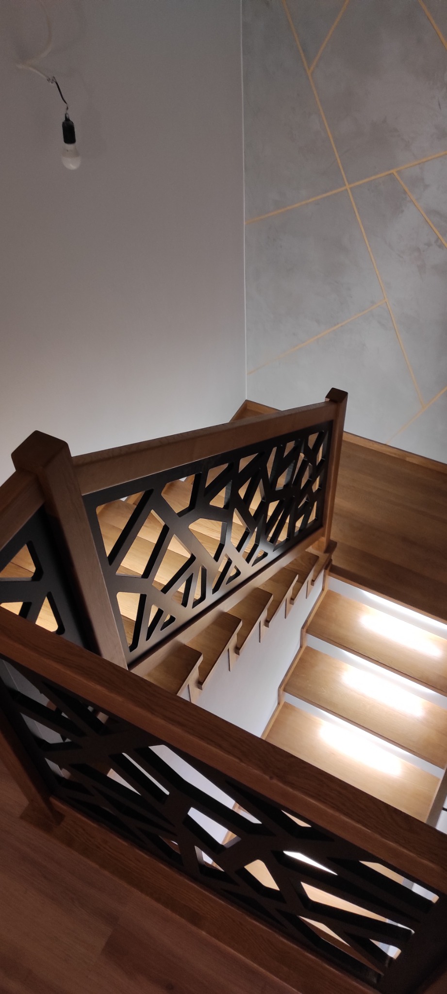 Drewniane schody z podświetleniem LED i nowoczesną, ażurową balustradą w domu w Szalowej, widok z góry.