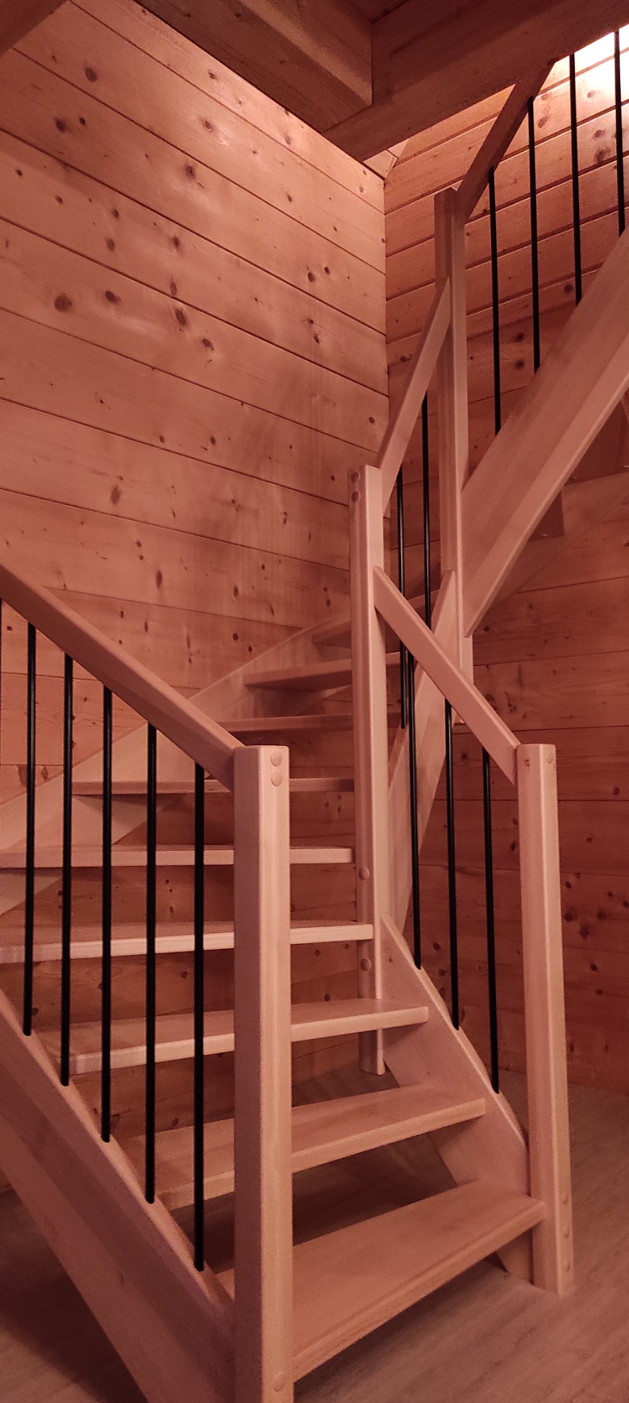 Jasne drewniane schody z czarnymi metalowymi balustradami w domu wykończonym boazerią.