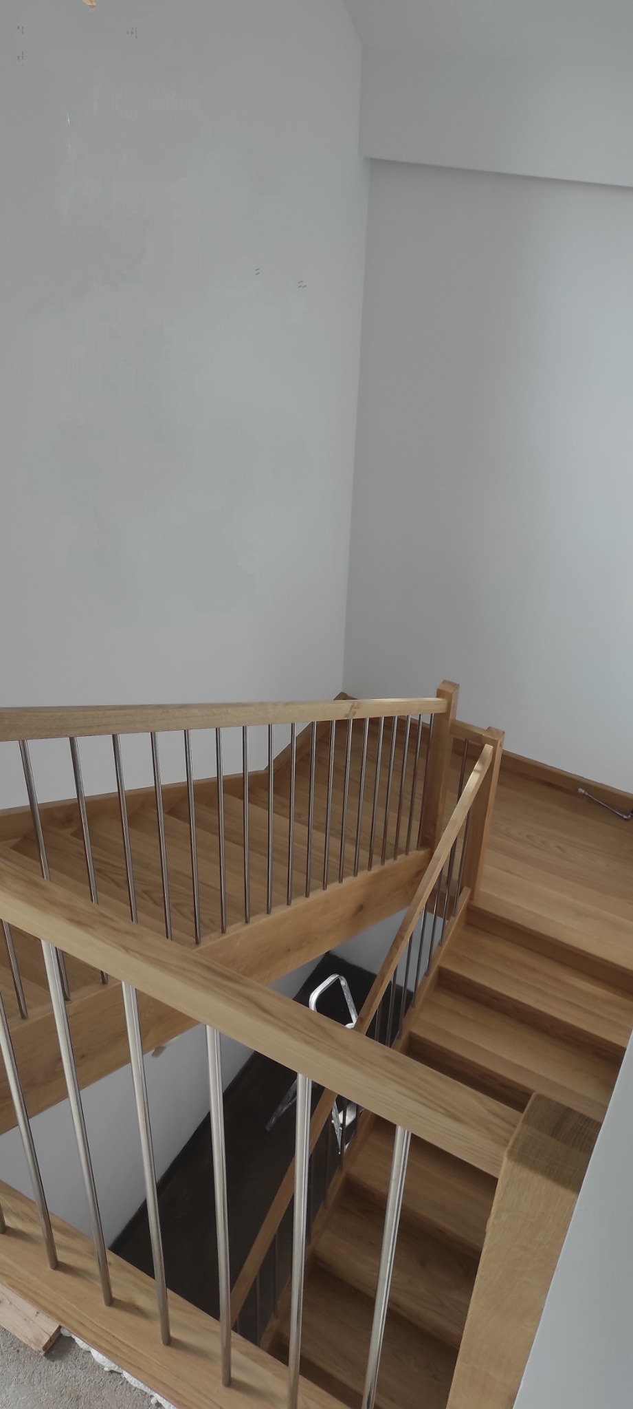 Jasne, drewniane schody z metalowymi balustradami, widok z góry, minimalistyczne wnętrze z białymi ścianami.