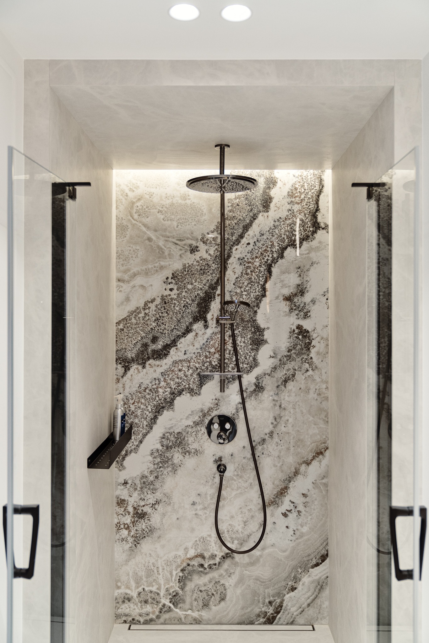 Nowoczesna kabina prysznicowa typu walk-in z deszczownicą, wykończona płytami imitującymi onyks, z czarnymi elementami armatury i szklanymi drzwiami.