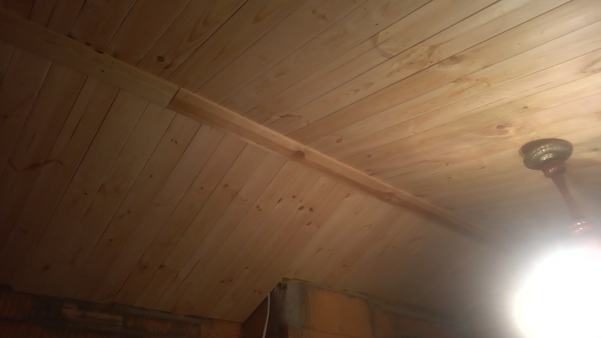 Drewniany sufit z widocznymi deskami i listwami wykończeniowymi, oświetlony lampą z kloszem w stylu retro.