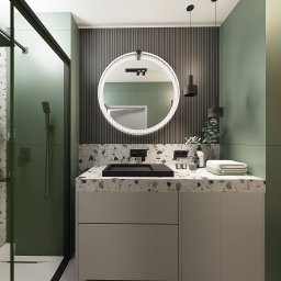 T.wórczo - Nowoczesna łazienka z okrągłym lustrem podświetlanym LED, czarną armaturą i umywalką nablatową na blacie z lastryko, zielone ściany i kabina prysznicowa ze szklanymi drzwiami.