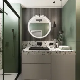 Nowoczesna łazienka z okrągłym lustrem podświetlanym LED, czarną armaturą i umywalką nablatową na blacie z lastryko, zielone ściany i kabina prysznicowa ze szklanymi drzwiami.