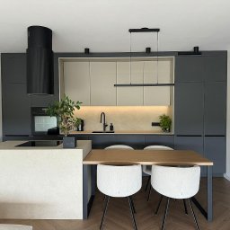 T.wórczo - Nowoczesna kuchnia w odcieniach szarości i beżu z drewnianym stołem i białymi krzesłami na parkiecie w jodełkę. Charakterystyczny okrągły okap nad płytą indukcyjną. Oświetlenie LED pod szafkami...