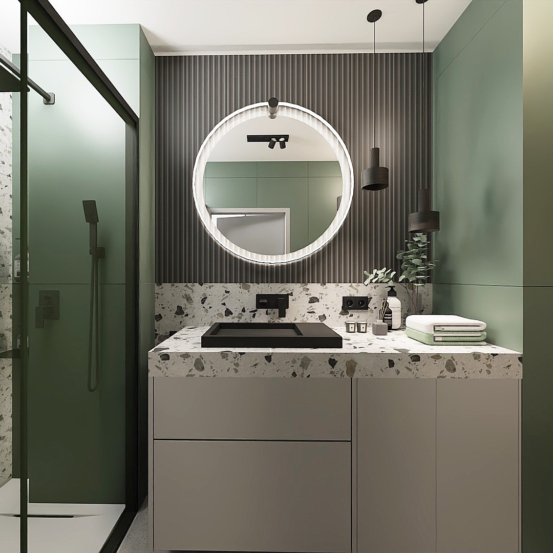 Nowoczesna łazienka z okrągłym lustrem podświetlanym LED, czarną armaturą i umywalką nablatową na blacie z lastryko, zielone ściany i kabina prysznicowa ze szklanymi drzwiami.