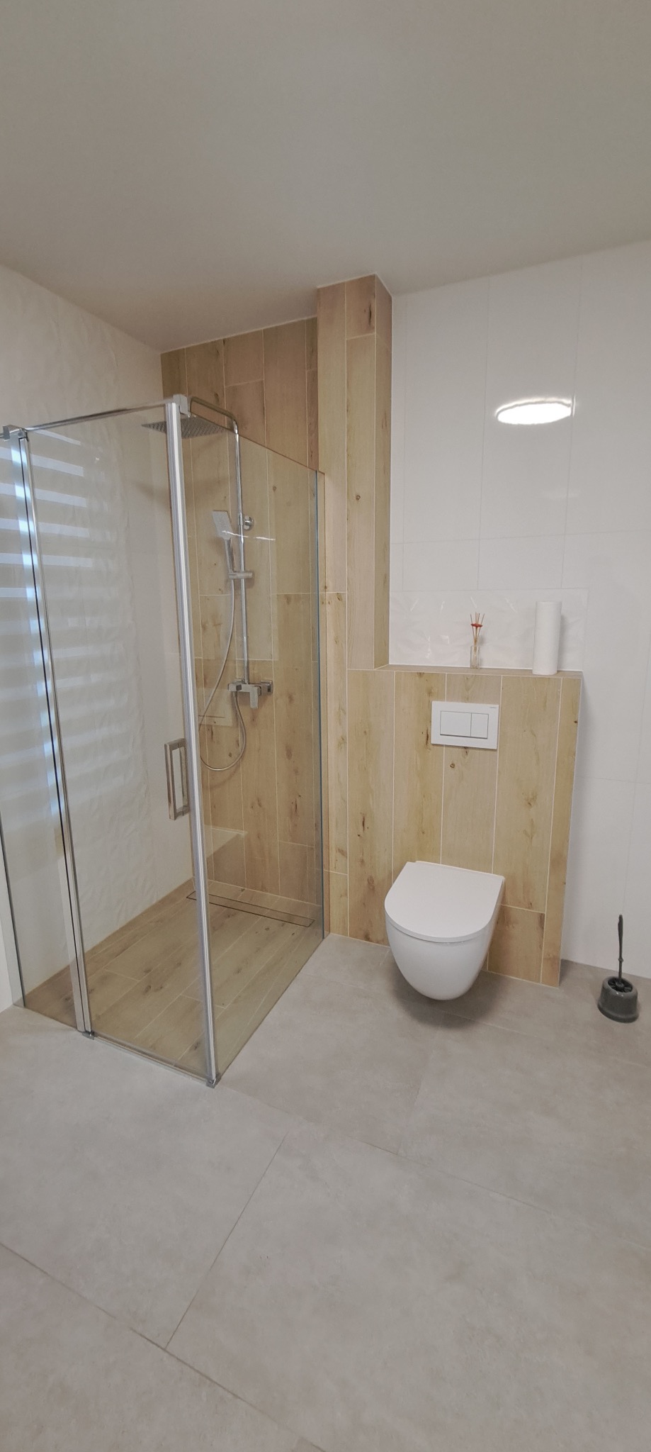 Nowoczesna łazienka z kabiną prysznicową typu walk-in, podwieszaną toaletą i płytkami imitującymi drewno na ścianach. Minimalistyczny design, szara podłoga.