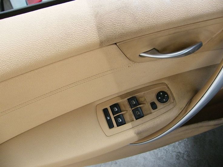 Beżowy panel drzwiowy samochodu z widocznymi śladami użytkowania i zabrudzeniami w okolicy klamki i przycisków sterowania szybami.
