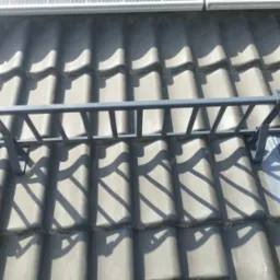 Szare dachówki ceramiczne z zamontowanym metalowym zabezpieczeniem przeciwśnieżnym i panelami słonecznymi w tle.